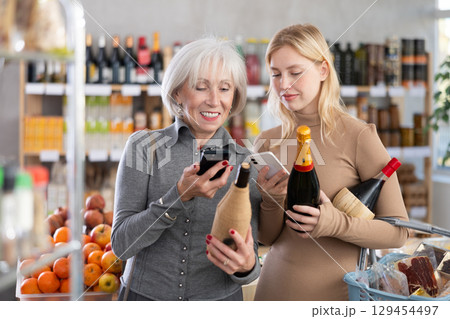 Girl and grandmother scan QR code, take reading wine and champagne label using phone camera in shop Girl and grandmother scan QR code, take reading wine and champagne label using phone camera in shop 129454497