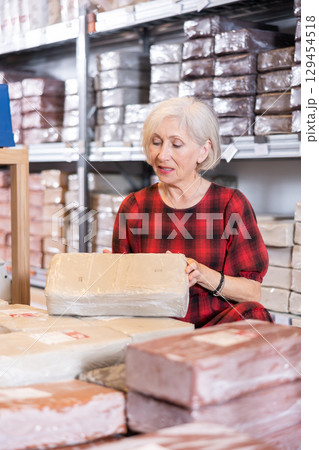 Elderly woman chooses pottery clay in shop 129454518