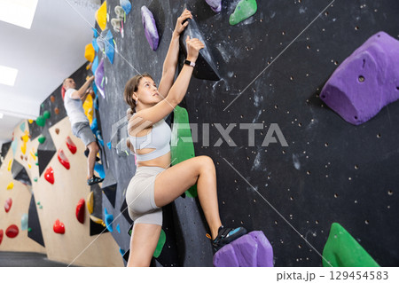 Young girl moving on bouldering wall at indoor climbing gym Young girl moving on bouldering wall at indoor climbing gym 129454583