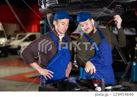 Two auto mechanics work together to diagnose an engine using a measuring device in car service center 129454640