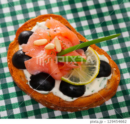 Toast with salmon, olives and creamy sauce on checkered textile 129454662