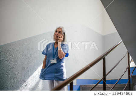 Mature nurse taking break during hospital shift, making phone call. 129454668