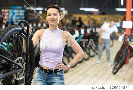 Young woman selects bicycle in sporting goods store, checking wheel quality 129454874
