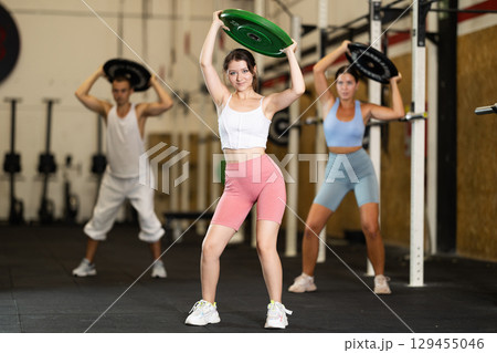 Closeup of athletic sports girl standing with plate of barbell in hands in fitness studio 129455046