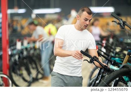 Young man choosing bicycle and checking bike handlebar quality in sport store Young man choosing bicycle and checking bike handlebar quality in sport store 129455070