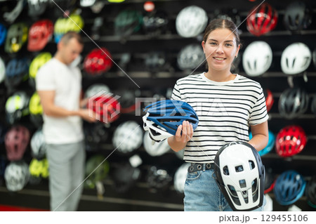Positive female customer choosing safe bicycle helmet in sports bike store Positive female customer choosing safe bicycle helmet in sports bike store 129455106