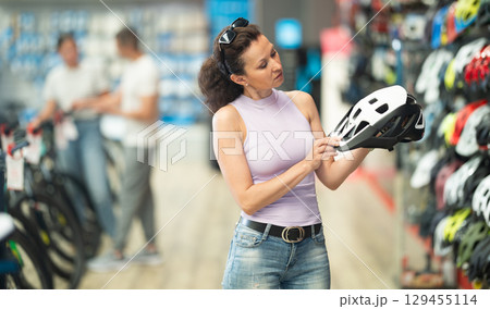 Adult woman choosing bicycle helmet in store Adult woman choosing bicycle helmet in store 129455114