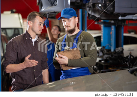 Owner of car explains to mechanic what needs to be repaired. Auto mechanic making notes on paper 129455131
