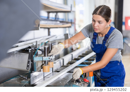 Glass workshop - girl works on machine for cutting aluminum profiles for windows Glass workshop - girl works on machine for cutting aluminum profiles for windows 129455202