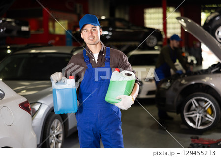 Positive male worker of car workshop holding full plastic cans Positive male worker of car workshop holding full plastic cans 129455213
