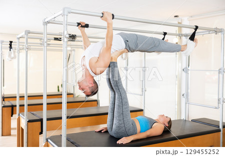 Man supports girl during Pilates classes on special sports equipment Man supports girl during Pilates classes on special sports equipment 129455252
