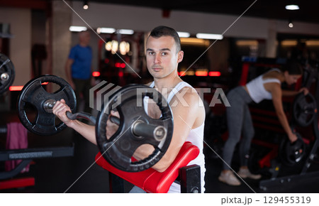 Sporty man performing set of exercises with barbell during intense workout 129455319