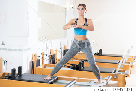 Woman doing pilates exercises lying on pilates workout machines in gym 129455371
