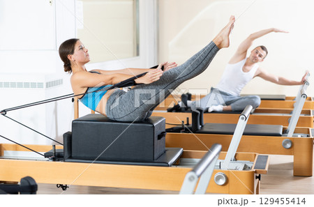 Sporty girl doing V-sit on Pilates reformer with box and straps 129455414