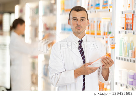 Young male pharmacist offering preparation in box Young male pharmacist offering preparation in box 129455692