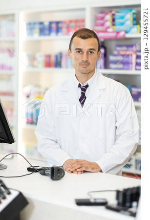 Man pharmacist stands in cash register area of pharmacy and waits for customers Man pharmacist stands in cash register area of pharmacy and waits for customers 129455721