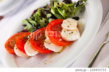 Caprese salad with fresh tomatoes, mozzarella cheese and basilic herb, dish of Italian cuisine 129455733