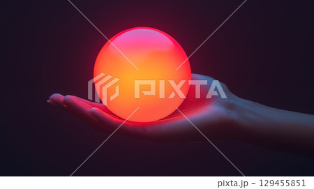 Glowing orb held in hand against dark background, futuristic technology concept with red and orange illumination 129455851