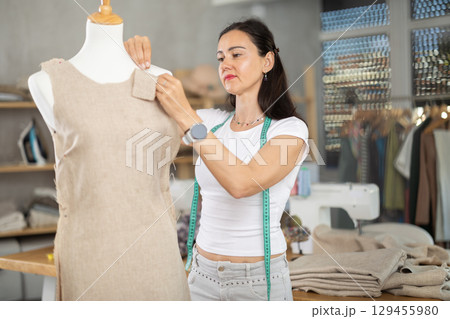 Woman tailor connects parts of dress on mannequin Woman tailor connects parts of dress on mannequin 129455980