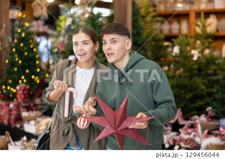 Young married couple chooses New Year toys and decorations in store or market Young married couple chooses New Year toys and decorations in store or market 129456044