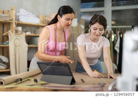 Using ruler and chalk, women tailor draws dress diagram scheme on paper 129456057
