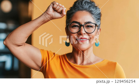 Mature woman in office with raised fist of empowerment, strength and women solidarity, International Womens Day concept 129456254