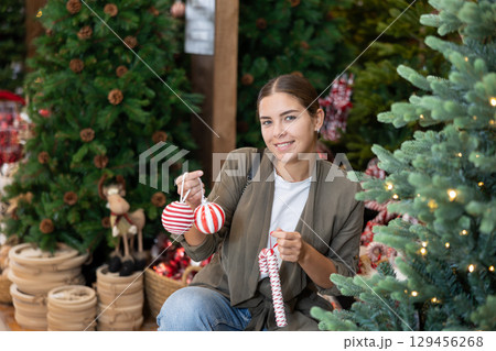 Girl buyer considers New Year and Christmas decorations ornaments for Christmas tree 129456268