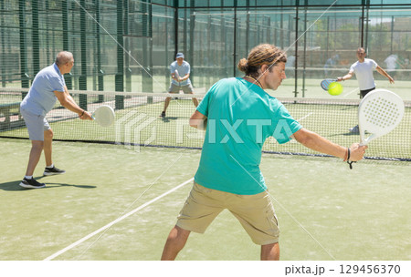 Men play padel on an outdoor tennis court. Hitting the ball with racket 129456370