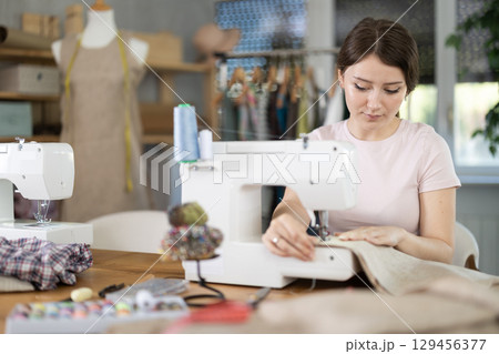 Woman seamstress sews on sewing machine in workshop 129456377