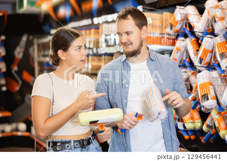 Married couple choose paint brush and paint roller together for their home renovation at hardware store 129456441