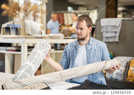 Male shopper carefully choose soft carpet in hardware store 129456559