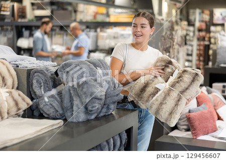 Female buyer carefully chooses warm blanket to create coziness in his apartment Female buyer carefully chooses warm blanket to create coziness in his apartment 129456607