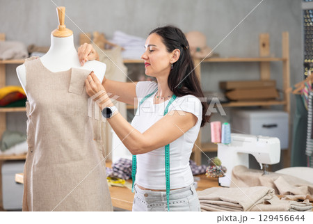 Woman dressmaker adjusts clothes on mannequin 129456644