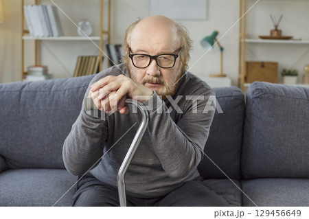 Mature sad man with thick beard feeling sleepy and tired, holding walking stick, focused at camera  129456649