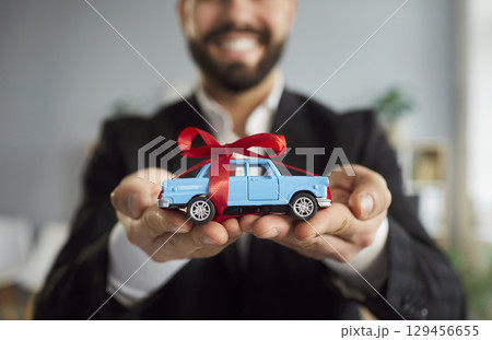 Close-Up Of Man Holding Toy Car With Red Ribbon 129456655
