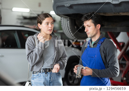 Man car mechanic talks with girl client in workshop and takes order. Man car mechanic talks with girl client in workshop and takes order. 129456659