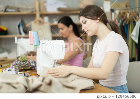 Two women tailor sews clothes in sewing machine Two women tailor sews clothes in sewing machine 129456680
