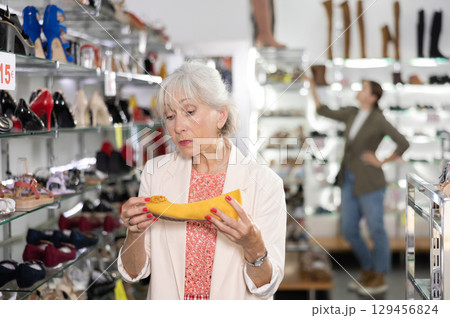 Elderly woman chooses ballet flats in shoe store 129456824