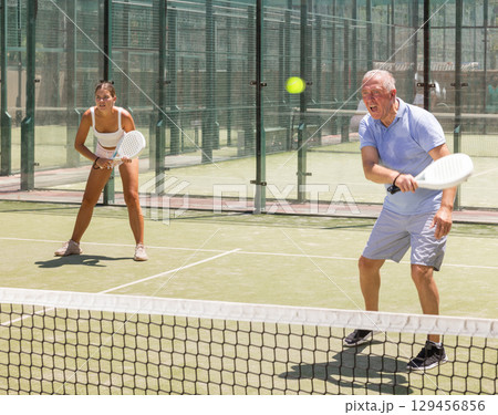 Elderly man and young woman playing doubles padel 129456856
