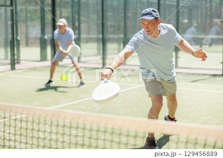 Elderly and adult men playing doubles padel 129456889