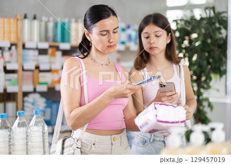 woman with her daughter scans a pack of pads on her phone 129457019