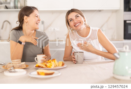 Two women having fun chatting and eating cupcake or pie in home kitchen 129457024
