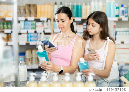 Woman with teen daughter in pharmacy scans QR code on mouthwash 129457198