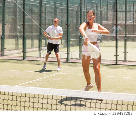 Young woman and man playing doubles padel 129457298