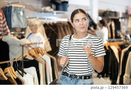Girl buyer noticed desired product in clothes store and happily smiles from upcoming purchase 129457369