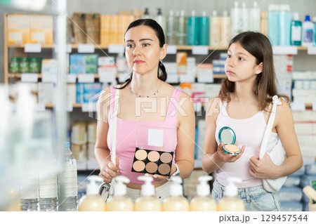 Mom and daughter choosing cosmetics in chemist's shop 129457544