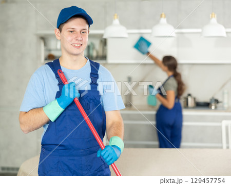 Smiling young professional worker of cleaning service sweeping office floor 129457754