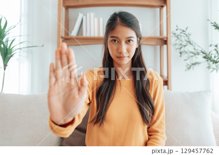 Young Asian woman with serious expression raising her hand stop gesture 129457762