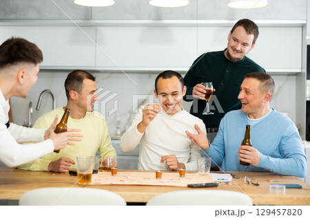Group of cheerful men engaged in alcohol-fueled board game 129457820