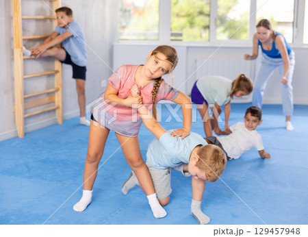 Children practicing in pair self-defence movements with female trainer supervision Children practicing in pair self-defence movements with female trainer supervision 129457948